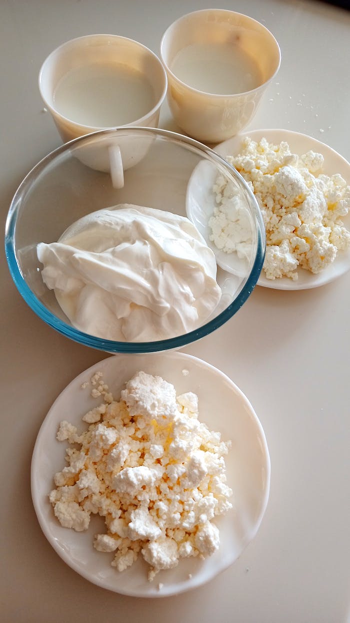 Close-up of cottage cheese and sour cream with cups of milk in a vertical layout.