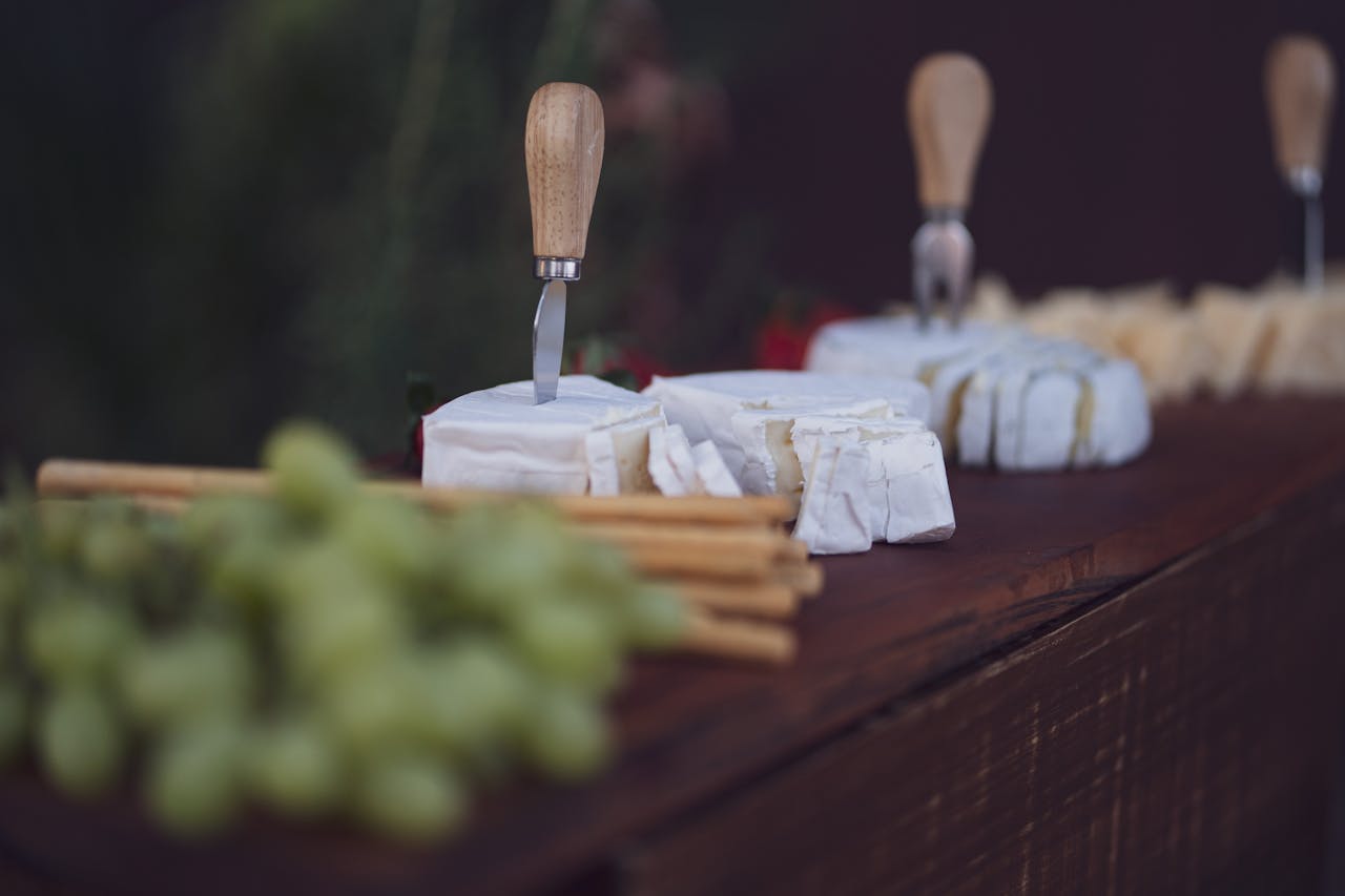 A beautifully arranged cheese board featuring various cheeses, grapes, and breadsticks with cheese knives.